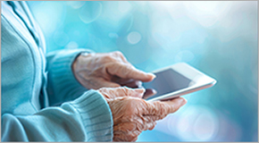 An elderly lady's hands on a smartphone with a blurred blue background, highlighting the use of technology by seniors.